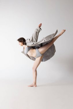 Esneklik. Gri arka planda, iç çamaşırı ve ceket giyen mutlu, genç bir kadın hareket ediyor. Sanat, hareket, hareket, esneklik, ilham konsepti. İlan ve tasarım için alanı kopyala
