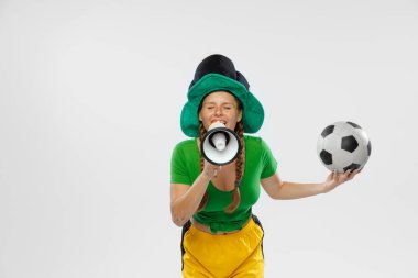 Win. Happy excited woman in green yellow football kit holding beer mug and football ball supports favorite team. Emotions, drinks, hobby, fans, competition, sport, oktoberfest concept. St. Patricks