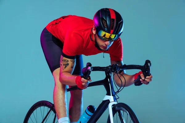 Training. Studio shot of professional cyclist in red sports uniform, goggles and a helmet on a blue background. Concept of active life, rest, travel, energy, sport. Copy space for ad