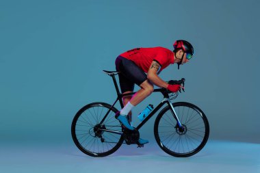 Bisiklet yarışı. Kırmızı spor üniformalı, gözlüklü ve mavi arka planda kask takan profesyonel bisikletçinin stüdyo fotoğrafı. Aktif yaşam, dinlenme, seyahat, enerji ve spor kavramı. İlan için alanı kopyala