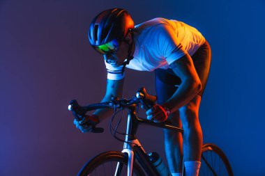 Closeup portrait of professional male cyclist in sports uniform, goggles and helmet on blue background in neon. Concept of active life, rest, travel, energy, sport. Copy space for ad. Moon light.