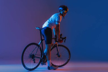 One male cyclist riding bicycle wearing cycling shorts and protective helmet isolated on dark blue background in neon. Concept of active life, rest, travel, energy, sport. Copy space for ad