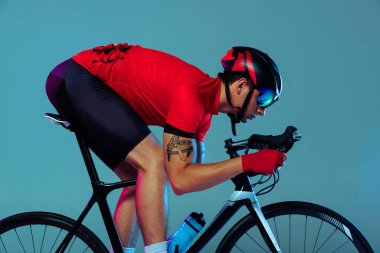 Training. Studio shot of professional cyclist in red sports uniform, goggles and a helmet on a blue background. Concept of active life, rest, travel, energy, sport. Copy space for ad