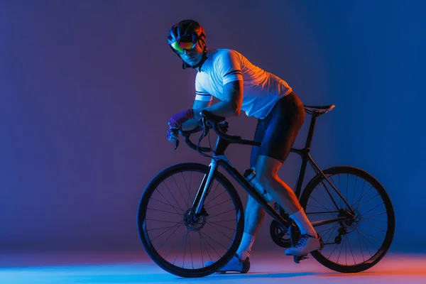 One male cyclist riding bicycle wearing cycling shorts and protective helmet isolated on dark blue background in neon. Concept of active life, rest, travel, energy, sport. Copy space for ad