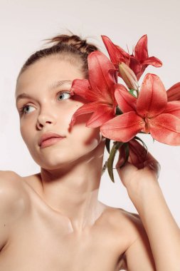 Kırmızı zambak. Beyaz stüdyo arka planında izole edilmiş çiçekli güzel bir genç kızın yakın plan portresi. Çıplak renk, diyet, kozmetik, doğal güzellik ve estetik kozmetik konsepti. Uzayı kopyala