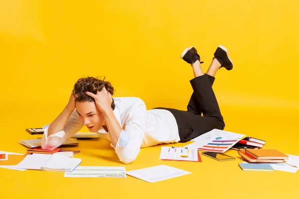 一个男孩 穿着商务服装的学生躺在地板上 在黄色的背景下独立做作业 考试准备工作 返回学校的概念 — 图库照片