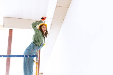 Cinsiyet kalıplarını yok etmek. Genç bir kadının canlı portresi, miğfer takan müteahhit inşaat alanında farklı iş aletleri kullanıyor. Cinsiyet eşitliği. Daire tadilatında çalışan bir kız. İş, iş