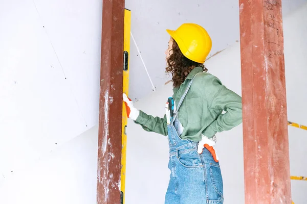 Destroying gender stereotypes. Live portrait of young woman, builder wearing helmet using different work tools at a construction site. Gender equality. Girl working at flat remodeling. Job, work