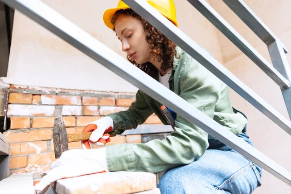 Destroying gender stereotypes. Live portrait of young woman, builder wearing helmet using different work tools at a construction site. Gender equality. Girl working at flat remodeling. Job, work