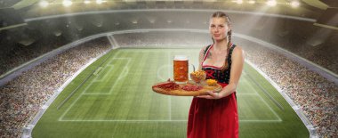 Atıştırmalık ve içecek. Sevimli, gülümseyen bir kadın, geleneksel bir Bavyera ya da Alman dirndl giyen garson kalabalık futbol stadyumunun arkasında koca bir kupa bira tutuyor. Spor etkinliği, Ekim festivali, futbol.