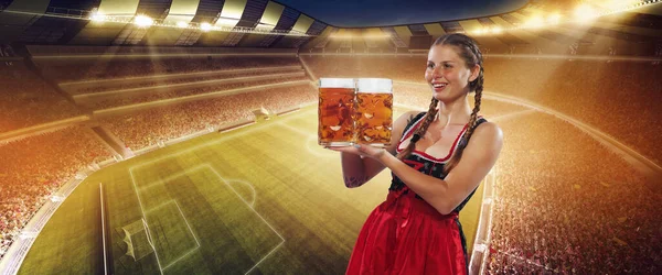 Mood. Adorable smiling woman, waitress wearing a traditional Bavarian or german dirndl holding big mug of beer over crowded football stadium background. Sport event, oktoberfest, soccer