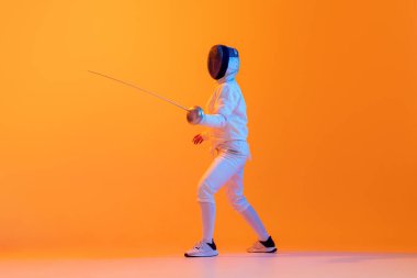 En garde. Studio shot of professional fencer in white fencing costume and mask in action, motion isolated on orange color background. Concept of sport, youth, activity, skills, achievements, ad.