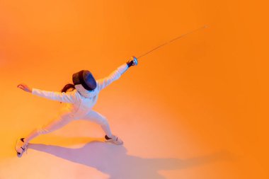 Aerial view of professional fencer in white fencing costume and mask in action, motion isolated on orange color background. Concept of sport, youth, activity, skills, achievements, ad.