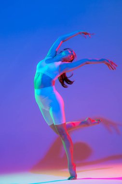 Dance. Studio shot of young flexible girl in fitness sport uniform practicing isolated on gradient pink-purple background in neon light. Modern sport, action, fitness, yoga, motion, youth concept.