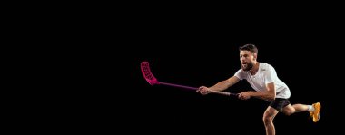 Spor üniforma giyen ve arka planda izole bir şekilde florbol oynayan genç adamın stüdyo fotoğrafı. Spor, hareket, hareket, rekabet. Beyzbol sopası ve topuyla antrenman. El ilanı