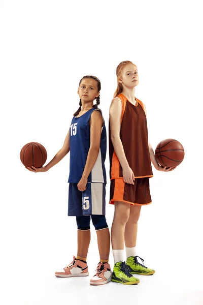 Rivals. Portrait of two young girls, basketball players posing with basketball ball isolated on white background. Concept of sport, team, enegry, skills. Junior game. Copy space for ad, text
