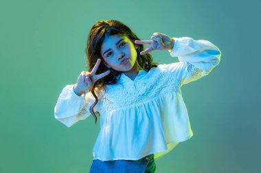 Güzel, güzel titreşimler. Mutlu küçük bir kız, günlük giysiler içindeki çocuk, beyaz neon ışıkta siyan renkli arka planda izole edilmiş. Çocuk duyguları, moda, güzellik kavramı, okula dönüş ve reklam.