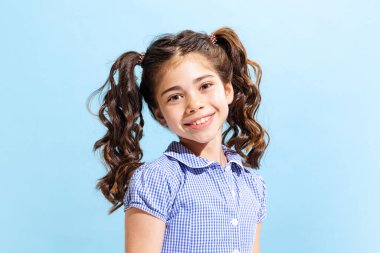 Cheerful shcoolgirl. Portrait of winsome little girl,school age kid in summer dress isolated over blue background. Concept of children emotions, happy childhood, fashion, beauty, back to school and ad