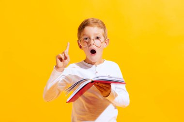 Brilliant idea. Portrait of cute little boy, emotional kid reading book with surprise isolated on bright yellow background with. Concept of child emotions, facial expression, fashion and ad.