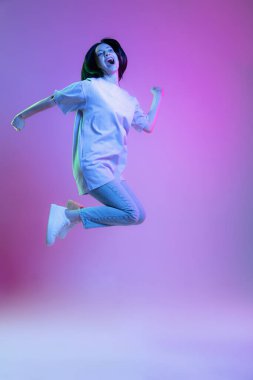 Zıplıyor, uçuyor. Sevimli bir kızın portresi, parlak, uzun siyah saçlı, mor arka planda, neon ışıkta izole edilmiş genç bir kadın. Güzellik, sanat, moda, gençlik, satış ve reklamlar. Mutluluk