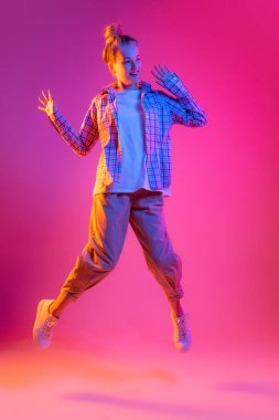 Flying. Young beautiful girl, student in casual style clothes isolated on magenta color background in neon light. Concept of beauty, art, fashion, youth, sales and ad, education, studying.