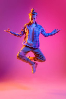 Meditation. Young beautiful girl, student in casual style clothes isolated on magenta color background in neon light. Concept of beauty, art, fashion, youth, sales and ad, education, studying.