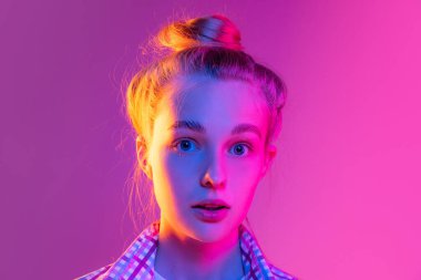 Mucizeyle. Genç, şaşkın bir kızın yakından çekilmiş yüzü. Öğrenci, neon ışıklarıyla mavi arka planda izole edilmiş kameraya bakıyor. Güzellik, sanat, moda, gençlik, satış ve reklam, eğitim kavramı