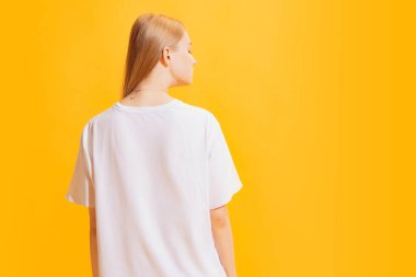 Genç ve güzel bir kızın arka planı, parlak sarı arka planda izole edilmiş günlük kıyafetli bir öğrenci. Güzellik, sanat, moda, gençlik, sağlıklı yaşam tarzı kavramı. Reklamlar, metinler, satış teklifleri için telif alanı.