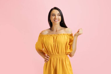 Gülümseyen genç bir kız, pembe arka planda izole edilmiş yaz sarısı elbiseli bir öğrenci. Güzellik, sanat, moda, gençlik, sağlıklı yaşam tarzı kavramı. Reklamlar ve metinler için kopyalama alanı