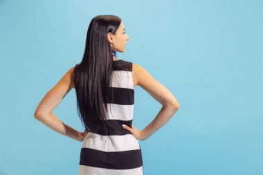 Retro tarzı. Yazlık çizgili elbisesiyle, açık mavi arka planda yalnız poz veren sevimli genç bir kadın. Güzellik, sanat, moda, gençlik kavramı. Reklam için kopyalama alanı. Arka plan