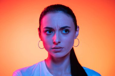 Güvensizlik. Genç ve çekici bir kızın turuncu renkli arka planda izole edilmiş neon ışığa bakan yüzü. Güzellik, sanat, moda, gençlik, satış ve reklam, eğitim kavramı