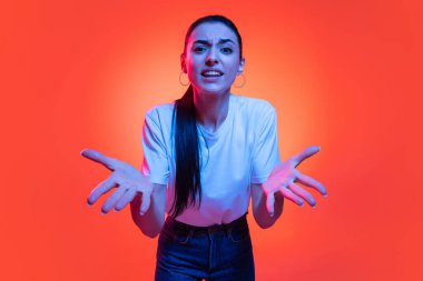 Yardım ve destek istiyor. Genç duygusal kız kameraya açık gözlerle bakıyor turuncu renkli arka planda, neon ışıkta izole edilmiş. Duyguların kavramı, yüz ifadesi, eğitim, öğrenim.