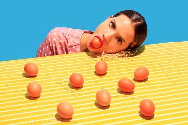 Mavi arka planda izole edilmiş parlak sarı masa örtüsü üzerindeki genç kadın ve yumurtaların yaratıcı görüntüsü. Ev hanımı. Yemek ve sanat fotoğrafçılığı. Antika, eski tarz. Tamamlayıcı renkler, reklam ve metin için alanı kopyala