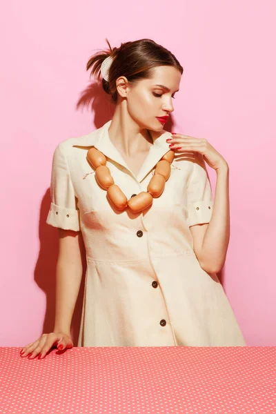 Food pop art photography. Portrait of young woman having necklace made from sausages. Creative food advertisement. Vintage, retro style. Complementary colors, Copy space for ad, text
