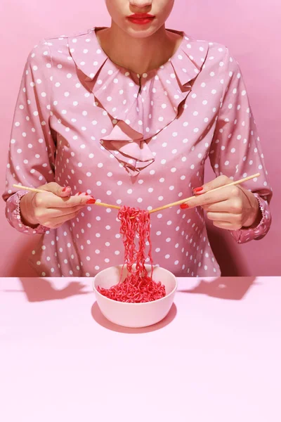 Colorful image of female hand and pink noodles isolated over pink background. Japanese cuisine, culture. Food pop art photography. Vintage, retro style. Complementary colors, Copy space for ad, text