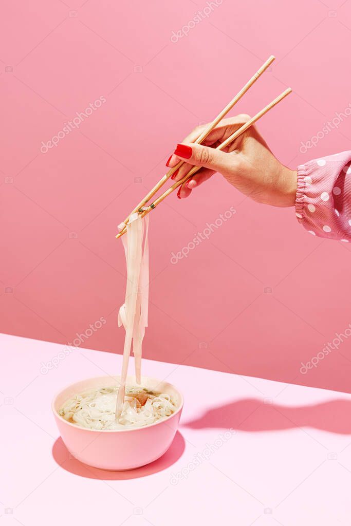 Spicy taste. Delicious image of noodles isolated over pink background. Eating japanese cuisine with chopsticks. Vintage, retro style. Complementary colors, Copy space for ad, text