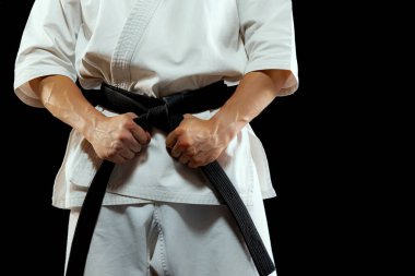 Power and strength. Cropped image of male karate fighter in white kimono and black belt in fighting stance on dark background. Sport, action, combat sports, ad concept