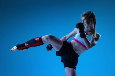 Bacak tekmesi. Sportif genç kızın atölye çekimi, MMA dövüşçüsü, mavi arka planda mavi ışıkta izole edilmiş hareket. Spor anlayışı, rekabet, eylem, başarılar. İlan için alanı kopyala.