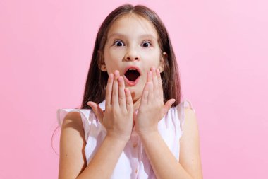 Şok oldum. Şaşkın küçük sevimli kız, pembe arka planda ağzı açık kameraya bakan çocuk. Çocuk duyguları, moda, güzellik, okul ve reklam kavramı.