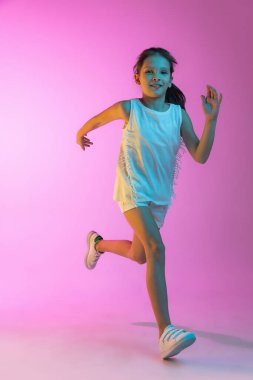 Koşmak. Mutlu küçük güzel bir çocuk, günlük kıyafetli liseli kız pembe arka planda izole edilmiş. Çocuk duyguları, moda, güzellik kavramı, okula dönüş ve reklam.