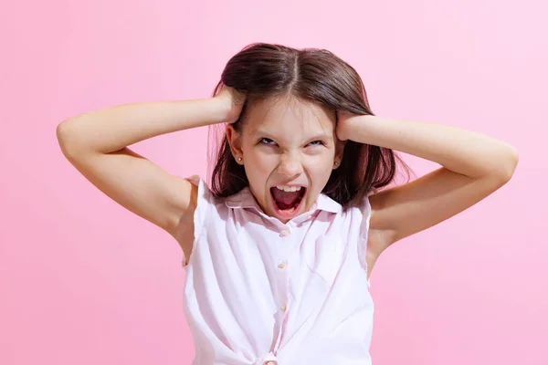 Irritation, anger. Negative emotions. Shouting little girl, kid wearing blouse isolated on pink background. Concept of facial expressions, fashion, beauty, school and ad concept.