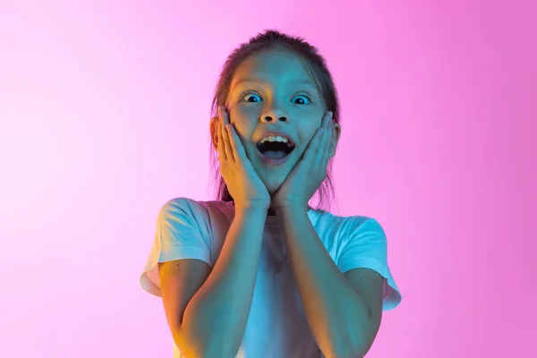 Wow, shock. Surprised little charming girl, kid looking at camera with open mouth isolated on pink background. Concept of children emotions, fashion, beauty, school and ad concept.