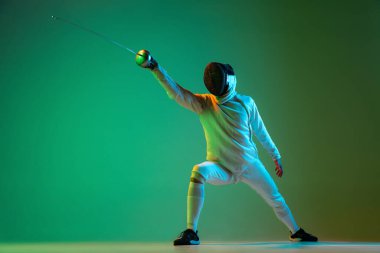 Stüdyo fotoğrafı, eskrim ustası, eskrim ustası, neon ışıkta yeşil arka planda izole edilmiş. Hareket halindeki atlet, motor. Reklam için kopyalama alanı.