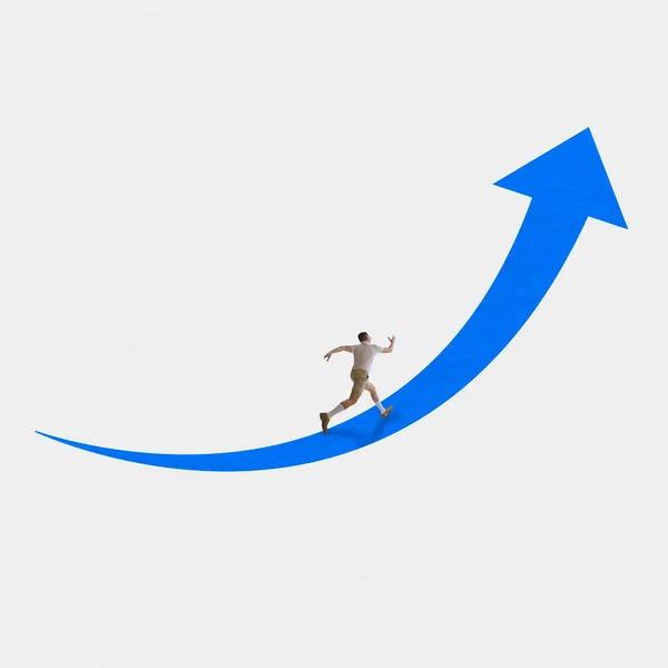 Going to your goal. Young man running forward towards his goal along the blue arrow over white background. Concept of business, psychology of success, finance, achievements.