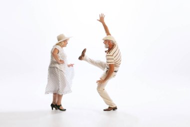 Timeless style and fashion. Dynamic portrait of retro style dancers, senior man and woman in vintage attire dancing swing isolated on white background. Concept of culture, art, music, style, ad