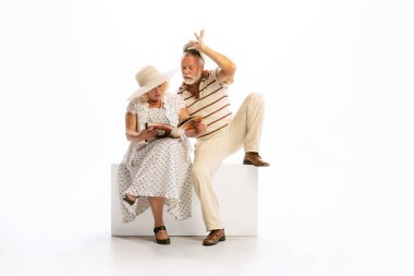 Flirt. Emotional senior man and woman in her 60s in vintage attire sitting together isolated on white background. Concept of relationship psychology, age, retro fashion, old generation