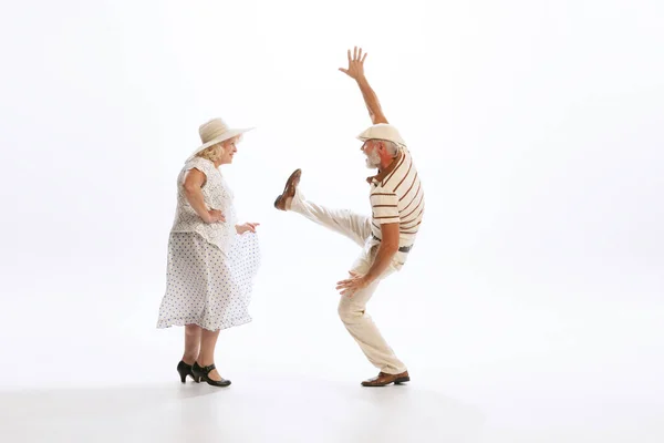 Timeless style and fashion. Dynamic portrait of retro style dancers, senior man and woman in vintage attire dancing swing isolated on white background. Concept of culture, art, music, style, ad