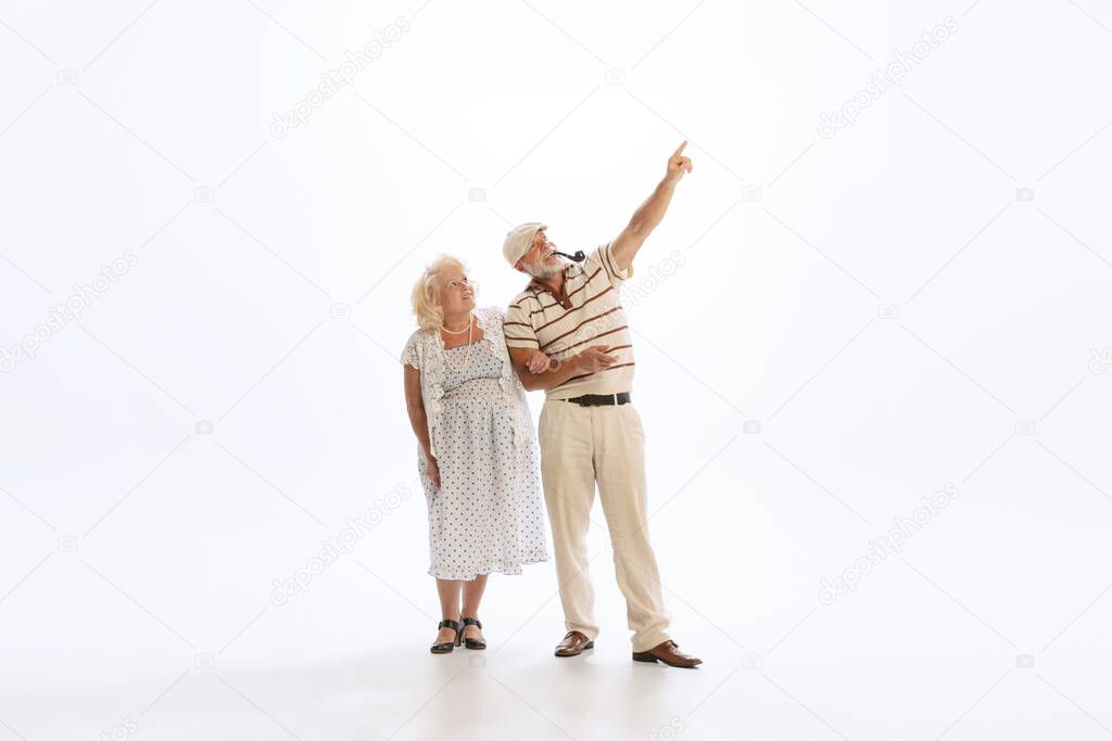 Couple in love. Portrait of retro style people, senior man and woman in vintage attire walking isolated on white background. Concept of relationship psychology, age, fashion