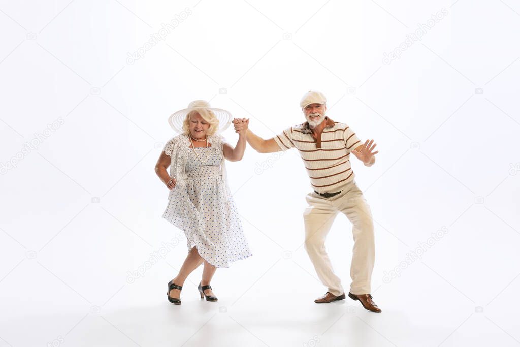 Timeless style and fashion. Dynamic portrait of retro style dancers, senior man and woman in vintage attire dancing swing isolated on white background. Concept of culture, art, music, style, ad