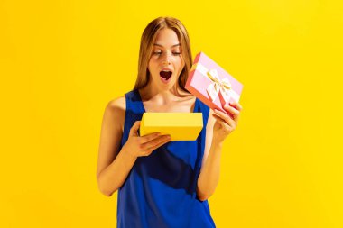 Surprise, happy womens day. Thrilled young beautiful blond girl holding gift box isolated on yellow background. Concept of positive emotions, holidays, inspiration, sales, ad.